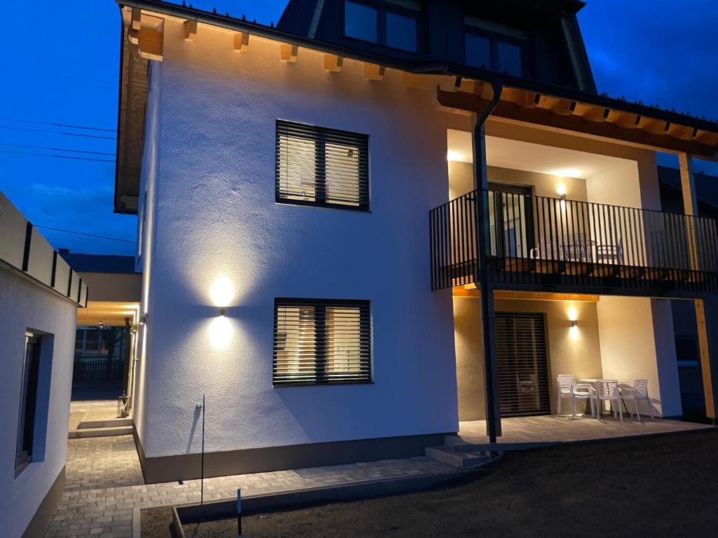 a white house with chairs and a balcony at night at Lake & Town Apartments Klagenfurt in Klagenfurt