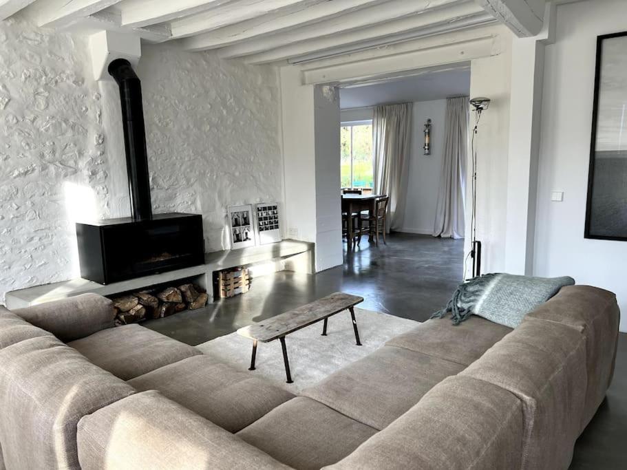 een grote bank in een woonkamer met een open haard bij Maison dans un village de charme au coeur de la forêt de Fontainebleau in Recloses