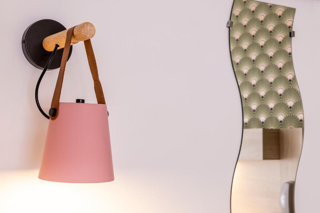 a pink lamp hanging on a wall next to a mirror at Hôtel de Lion sur Mer in Lion-sur-Mer