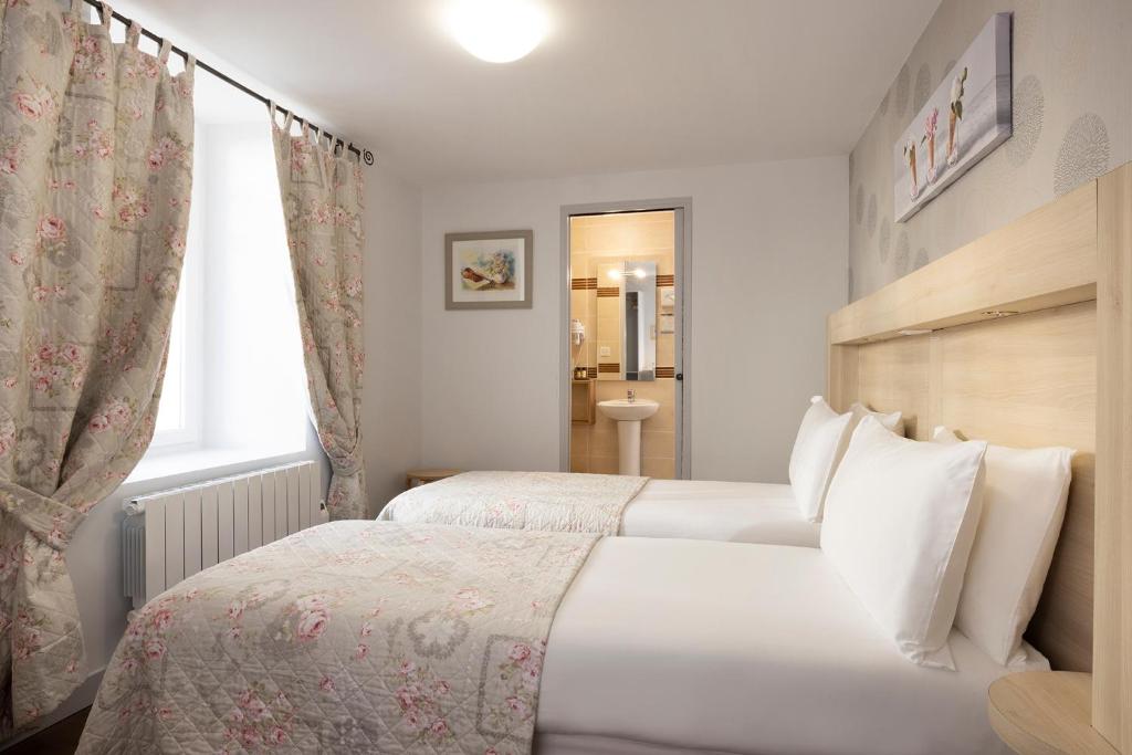 two beds in a hotel room with a window at Hôtel de Lion sur Mer in Lion-sur-Mer