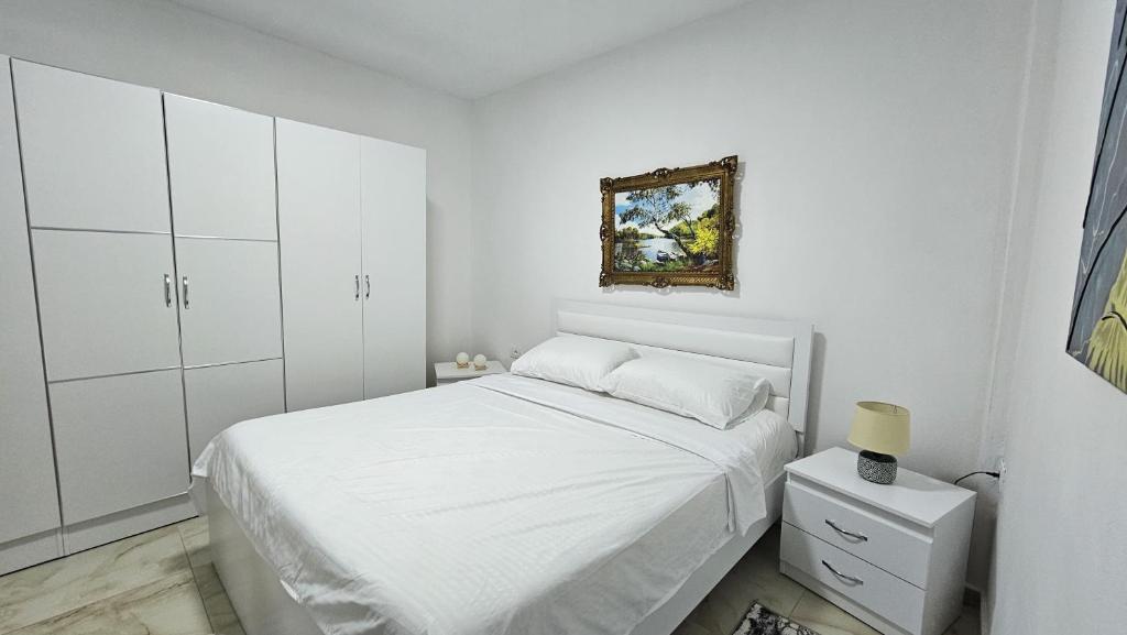 een witte slaapkamer met een bed en een foto aan de muur bij Guesthouse Albi in Berat