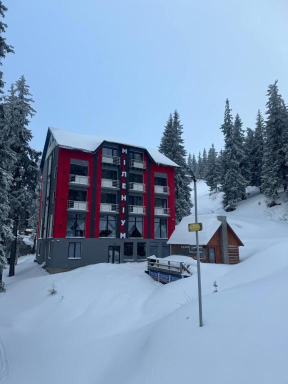 un grand bâtiment rouge dans la neige avec des arbres dans l'établissement Готель Міленіум, à Dragobrat