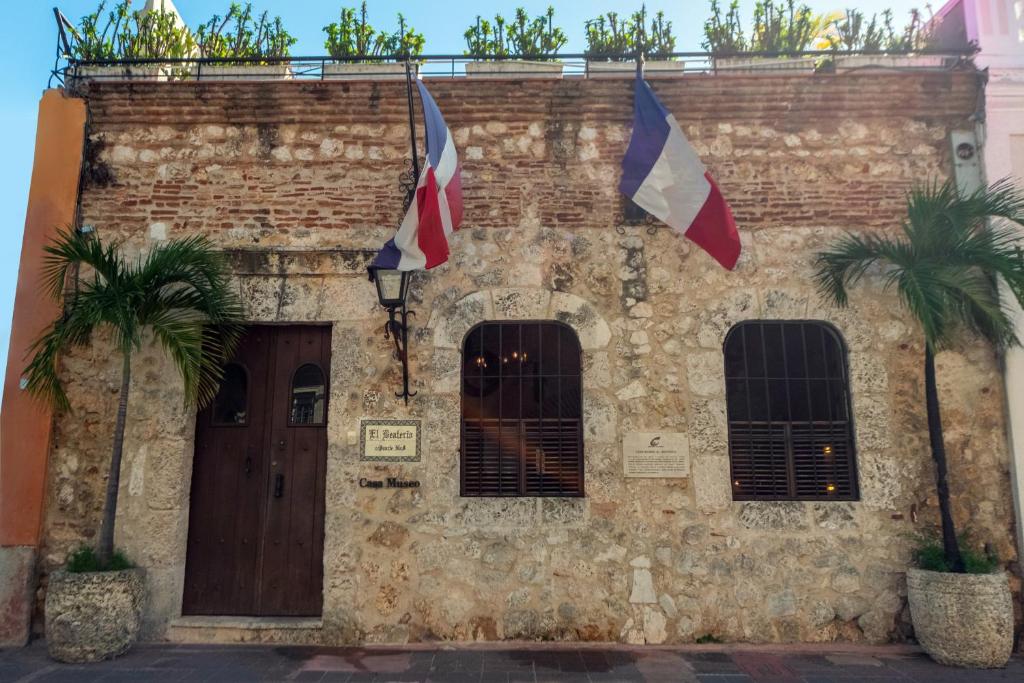 a brick building with flags on it with two palm trees at El Beaterio Casa Museo in Santo Domingo