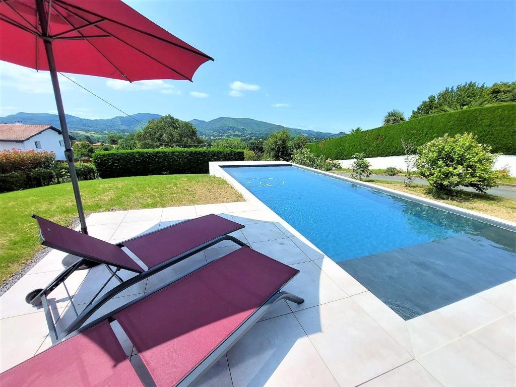 een rode parasol en een stoel naast een zwembad bij LE GARCIA villa au calme et vue sur les montagnes in Urrugne