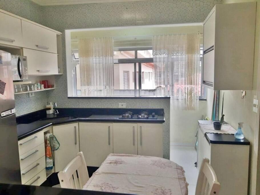 a kitchen with white cabinets and a table and a window at Apartamento na aviação in Praia Grande