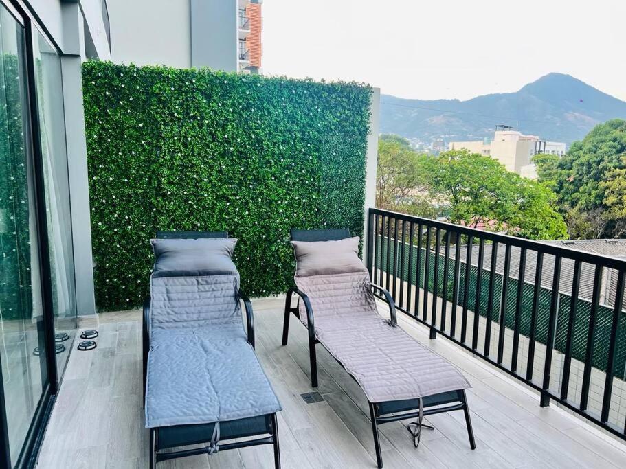 a balcony with two chairs and a green hedge at Elegante y acogedor apartamento en el corazón de San Salvador in San Salvador