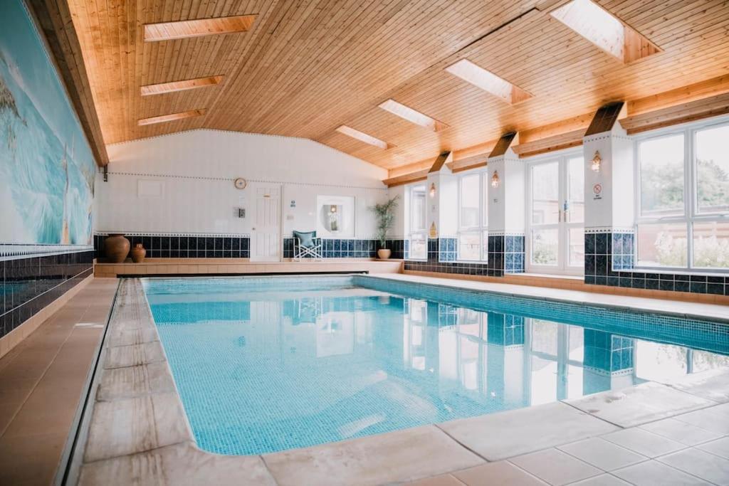 a large swimming pool with a wooden ceiling at Vast, Elegant Home with Indoor Pool & Sauna near Popular Golf Course in Kington
