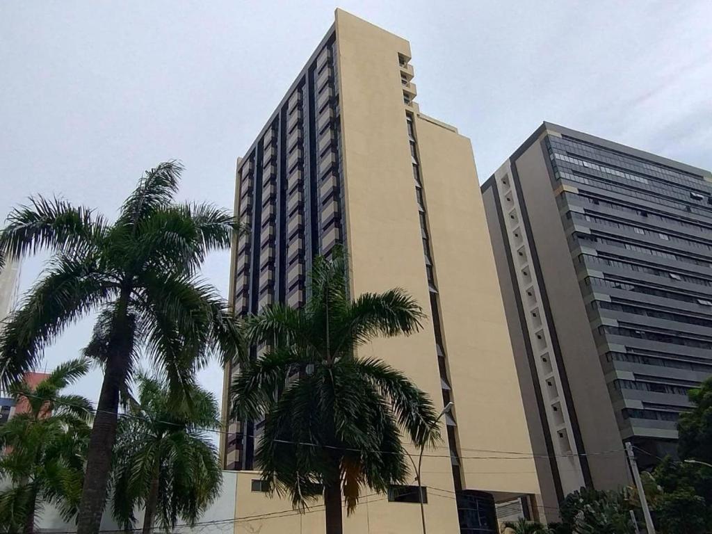 a tall building with palm trees in front of it at Athenas Suites By BnbHost in Salvador