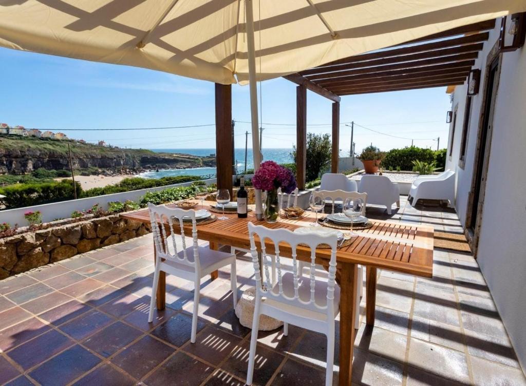 uma mesa de madeira e cadeiras num pátio com um guarda-sol em VIlla São Lourenço by AcasaDasCasas em Ericeira