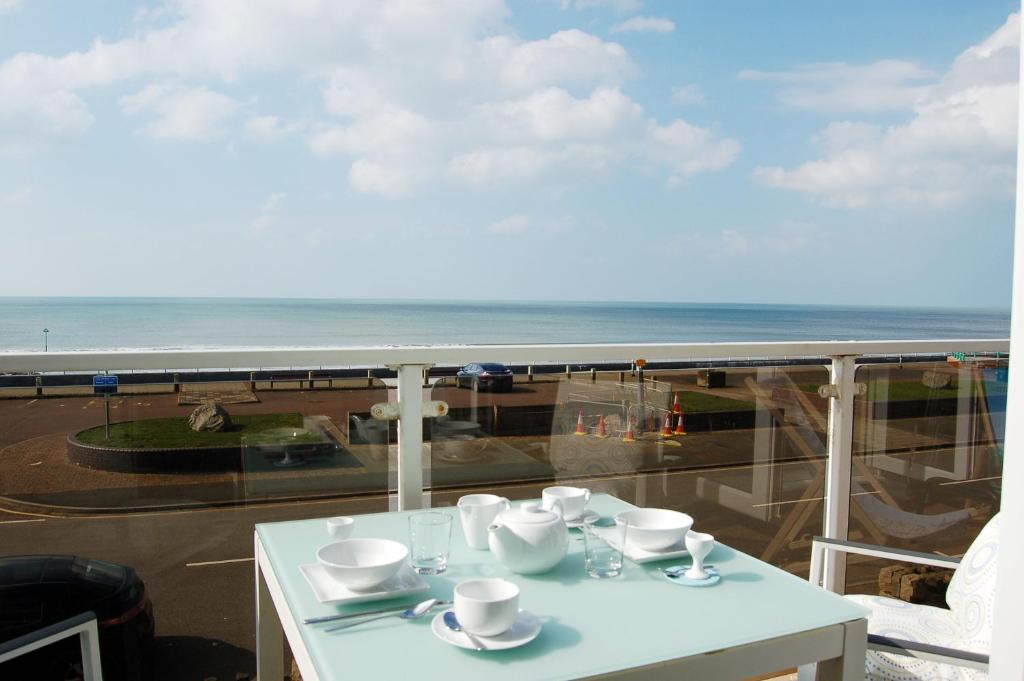 a table with cups and saucers on a balcony with the ocean at Sunset Bay Beach House in Tywyn in Tywyn
