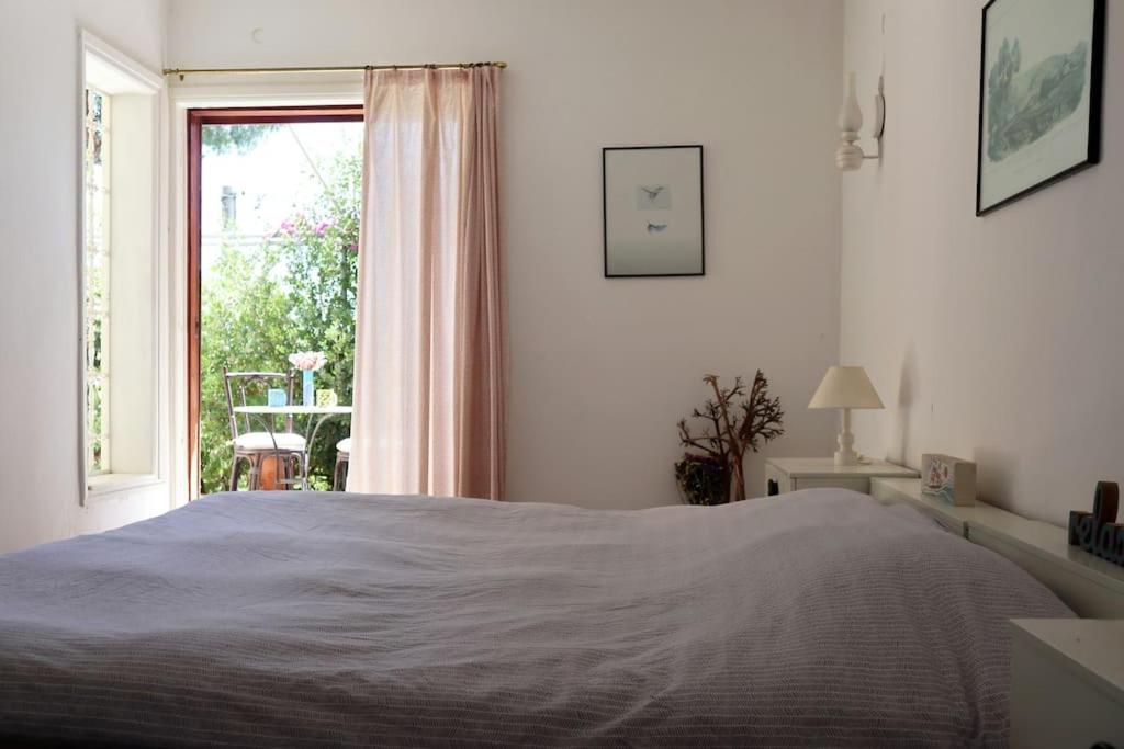 a white bedroom with a bed and a window at Sunny summer house with sea view in Koropíon