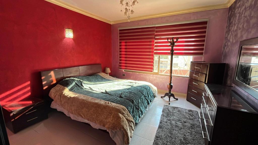 een slaapkamer met rode muren en een bed en een raam bij Tarawneh & Thawabi in Amman