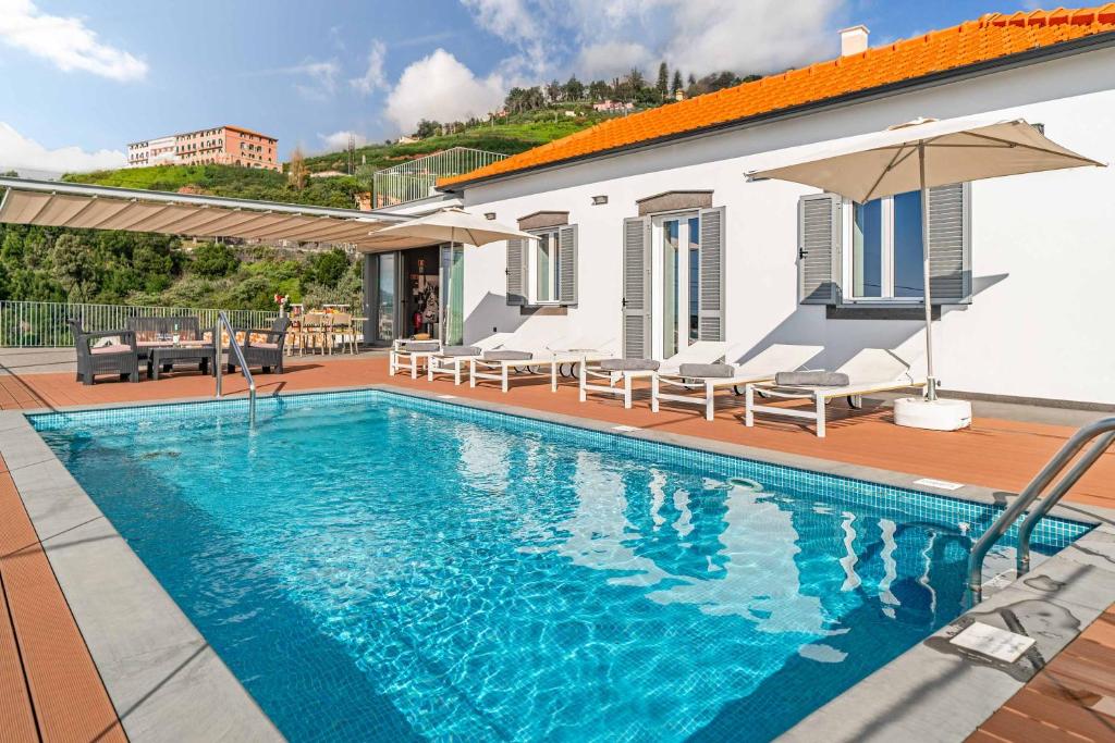 a swimming pool with chairs and an umbrella next to a house at Villa da Portada in Funchal