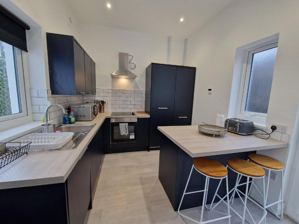cocina con fregadero y 2 taburetes en 5 Bedroom modern home with parking. Near Brecon Beacons & Bike Park Wales, en Merthyr Tydfil