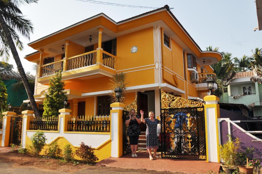 貝瑙利姆的住宿－敏瑞雅旅館，两个人站在一个黄色房子前面