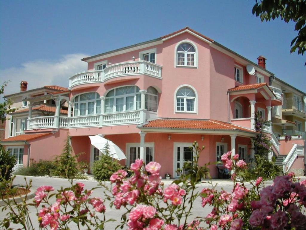 Hotel Villa Vera 2 في فاجانا: منزل وردي مع الكثير من الزهور الزهرية