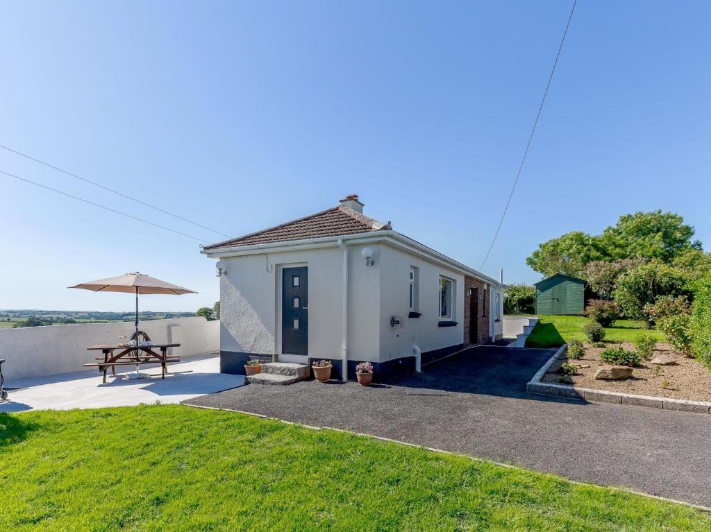 ein kleines weißes Haus mit einem Picknicktisch und einem Sonnenschirm in der Unterkunft 3 bed property in Bude 78213 in Ashwater