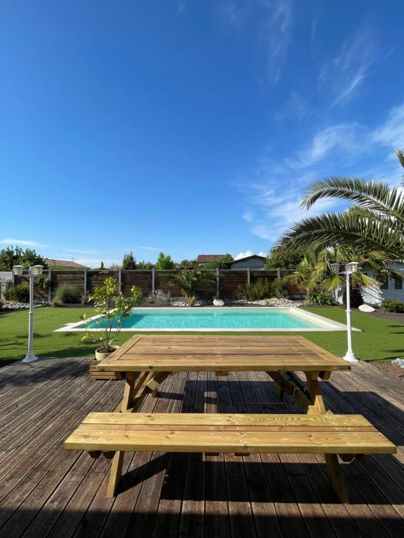 a wooden deck with a picnic table and a pool at Charmante Maison entre châteaux et océan in Cussac-Fort-Medoc