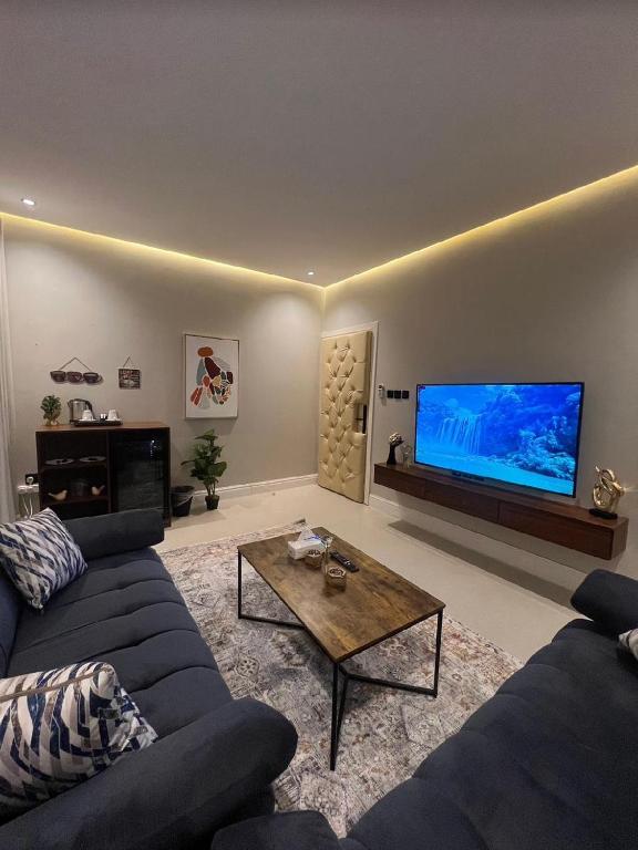 uma sala de estar com um sofá azul e uma televisão de ecrã grande em شقق سمارت انترى بالملقا em Riyadh