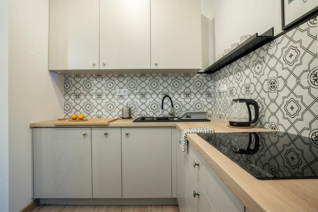a kitchen with white cabinets and a black and white tile wall at Apartament Gold Próchnika 9 in Łódź