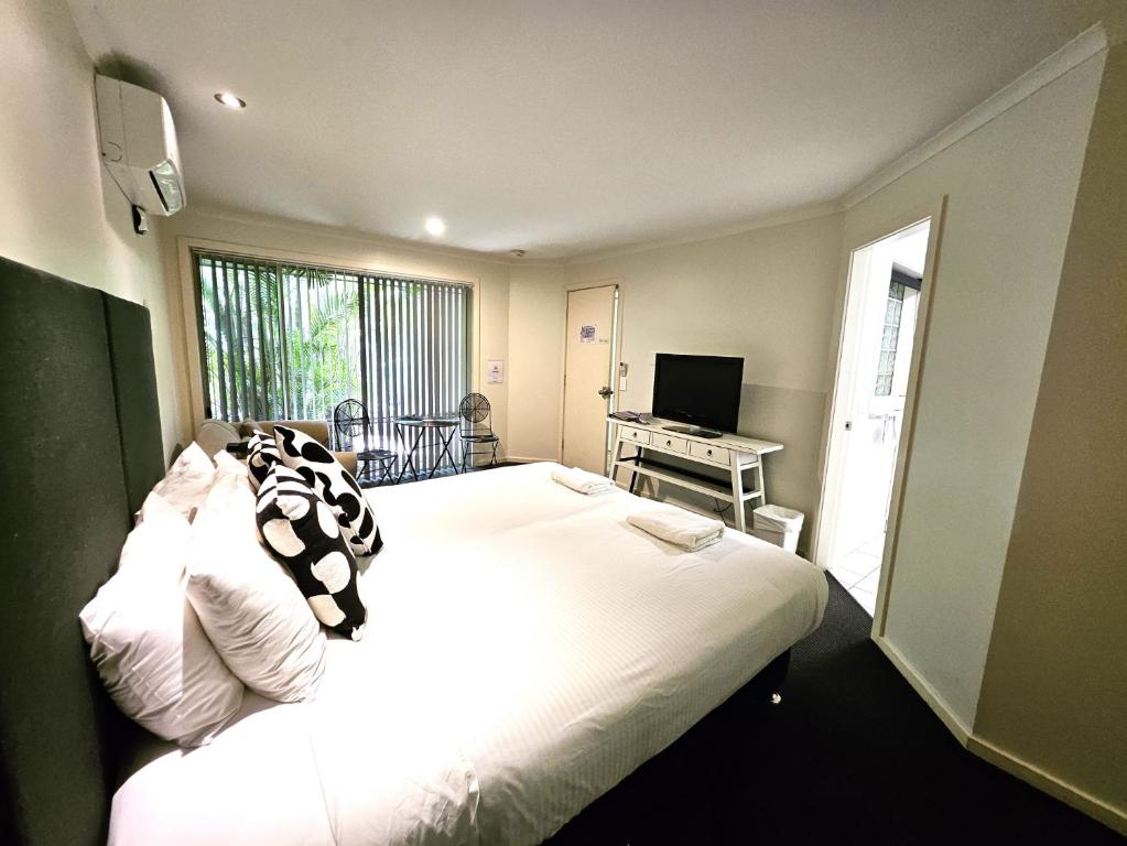 Un dormitorio con una gran cama blanca y un televisor. en Little Diggers, en Coffs Harbour