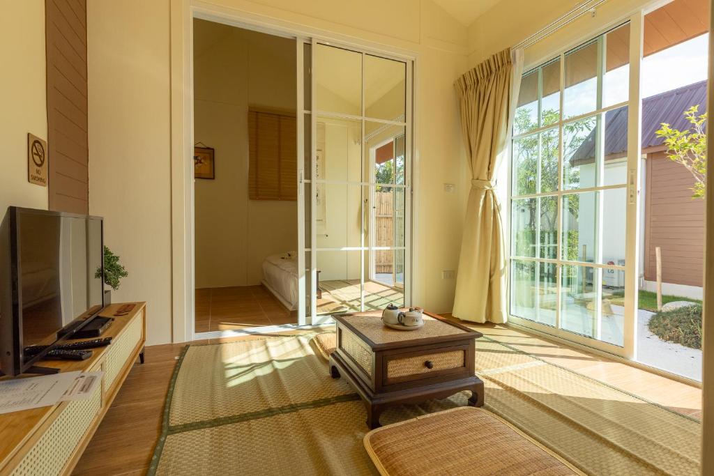 een woonkamer met een tv en een groot raam bij เรียวกัง ปาร์ค รีสอร์ท สไตล์ญี่ปุ่น Ryokan Park Resort in Ban Nam Dam