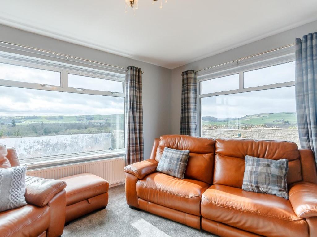 a living room with a leather couch and two windows at 3 Bed in Dumfries 77430 in Auldgirth
