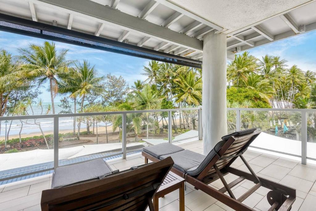 a porch with two chairs and a balcony with palm trees at Aspen - Beachfront Bliss at The Drift in Palm Cove