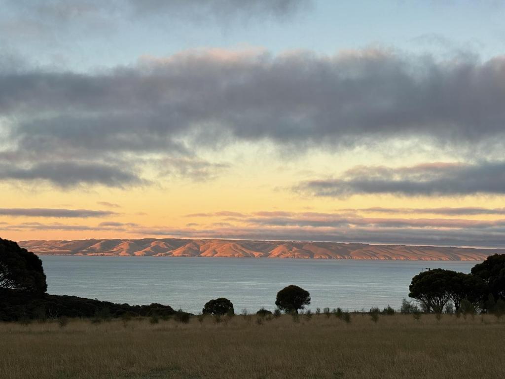 a sunset over the water with mountains in the background at Ocean Yakka, Kangaroo Island in Penneshaw