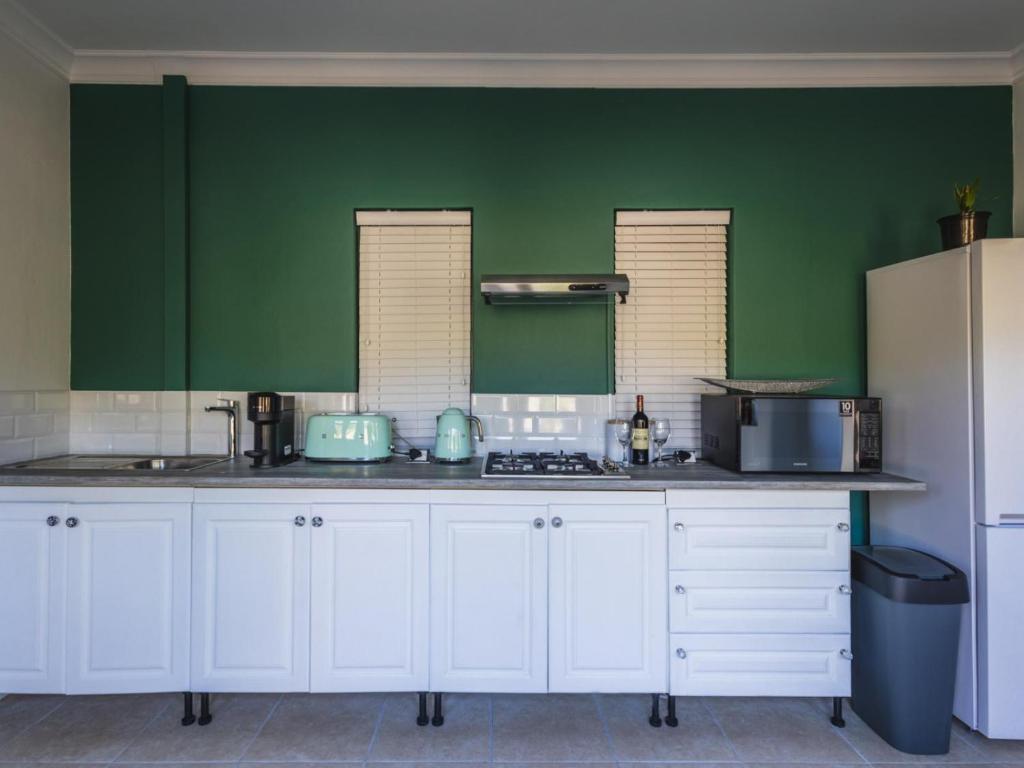 una cocina con armarios blancos y una pared verde en Cliffside Suites en Plettenberg Bay