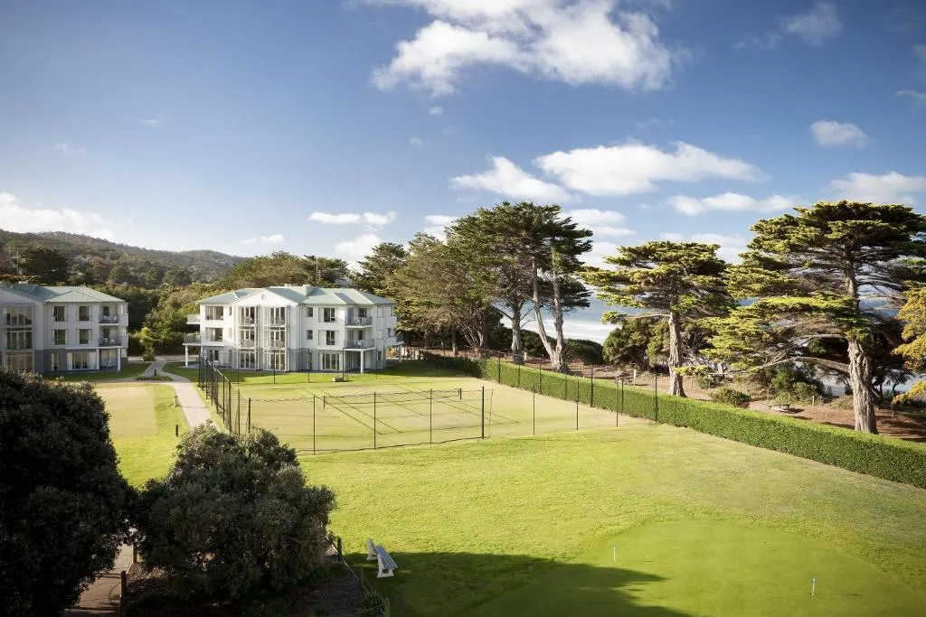 Tennis courts and white apartment buildings among pines, with the sea behind