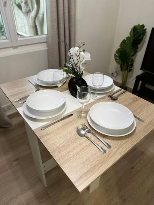 a wooden table with plates and wine glasses on it at Charmante maisonnette cosy près de Paris in Deuil-la-Barre