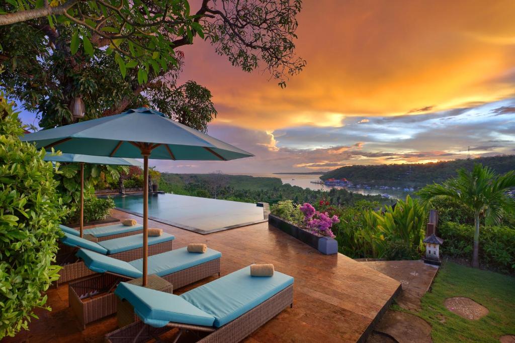 eine Terrasse mit Stühlen und einem Sonnenschirm mit Aussicht in der Unterkunft The Acala Shri Sedana in Nusa Lembongan