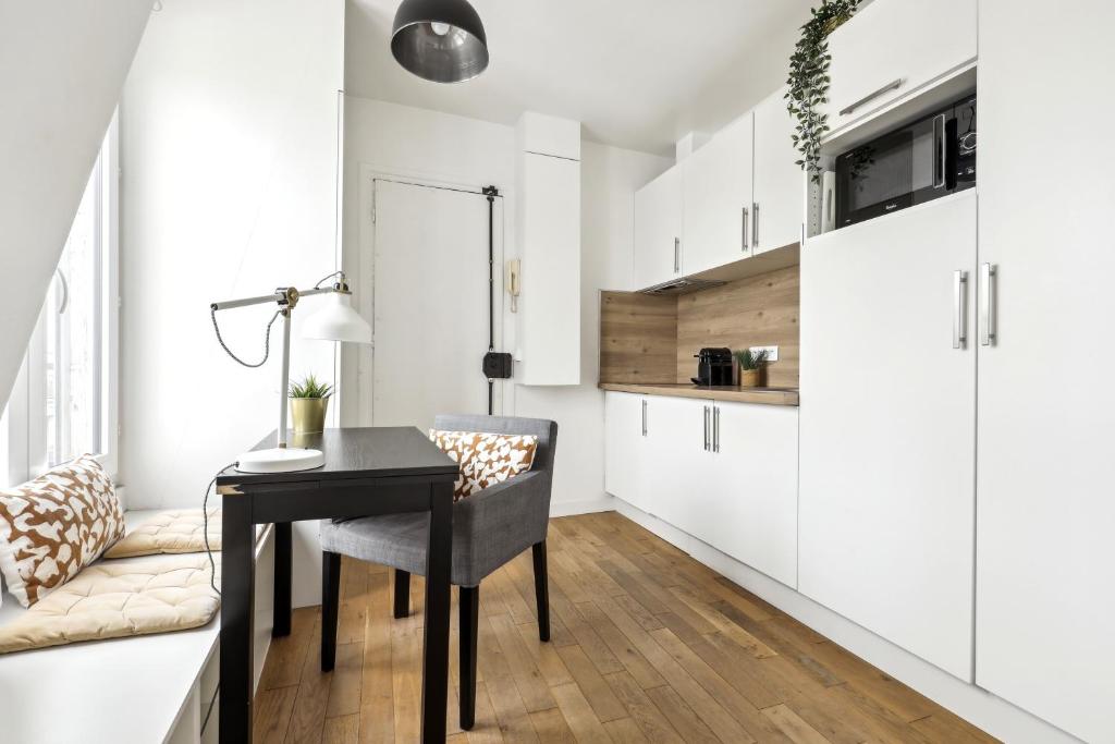 une cuisine avec des placards blancs et une table avec une chaise dans l'établissement Bright top floor studio near Pere Lachaise, à Paris