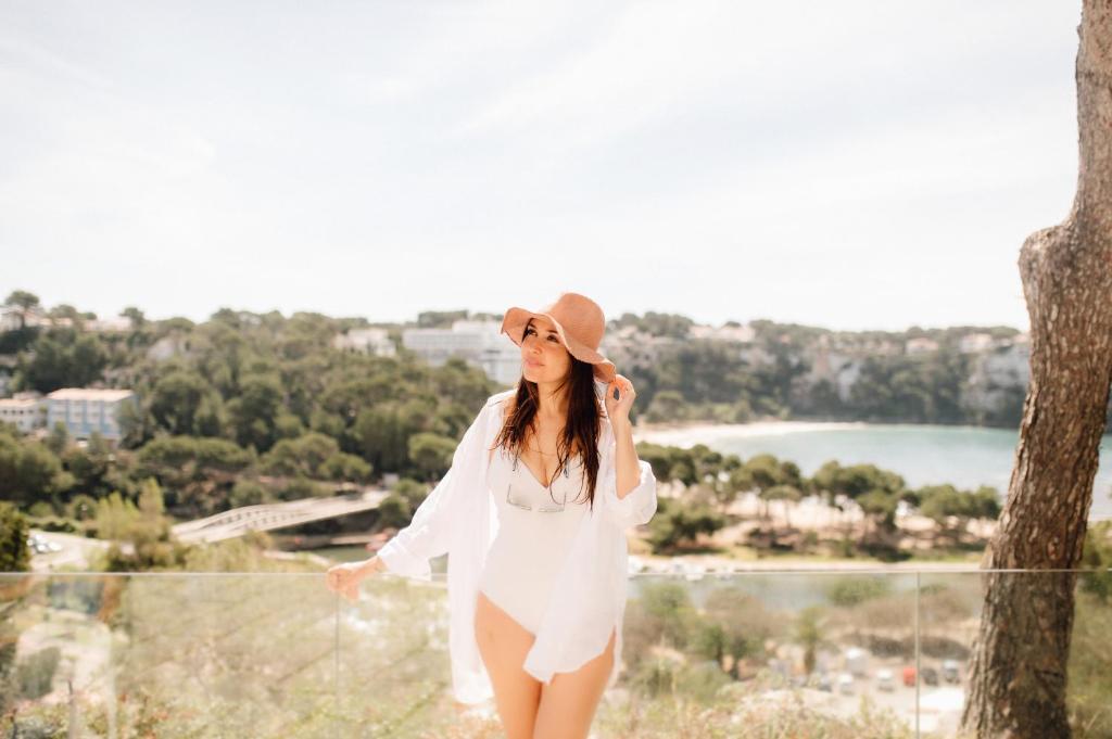a woman in a white dress and hat talking on a cell phone at Comitas Floramar in Cala Galdana