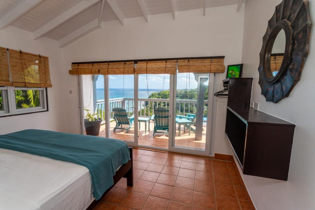 a bedroom with a bed and a balcony with a table and chairs at Hodges Bay House in Calibishie