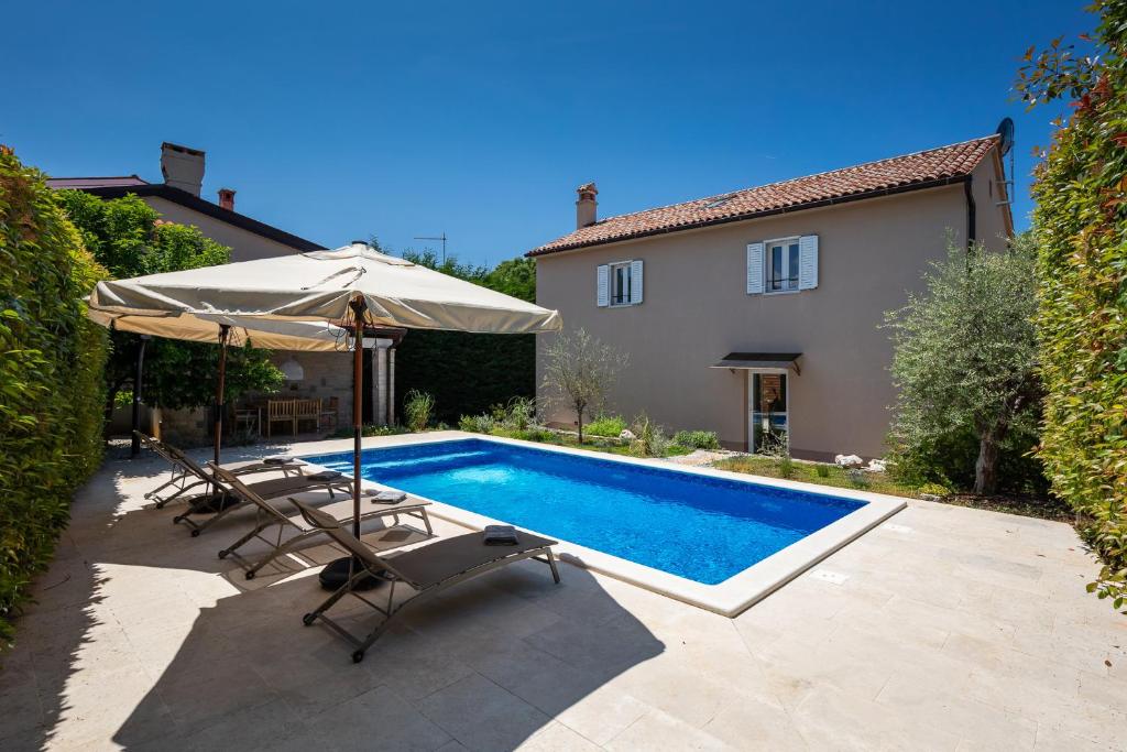 una piscina con sillas, una sombrilla y una casa en Villa Vin with 2 bedrooms and pool in Porec, en Nova Vas