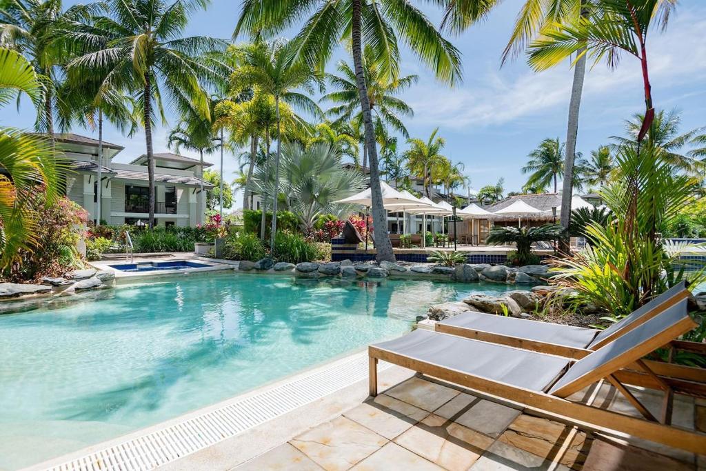 uma piscina com palmeiras e uma casa em Poolside Relaxation - Resort Retreat with Beach Access em Port Douglas