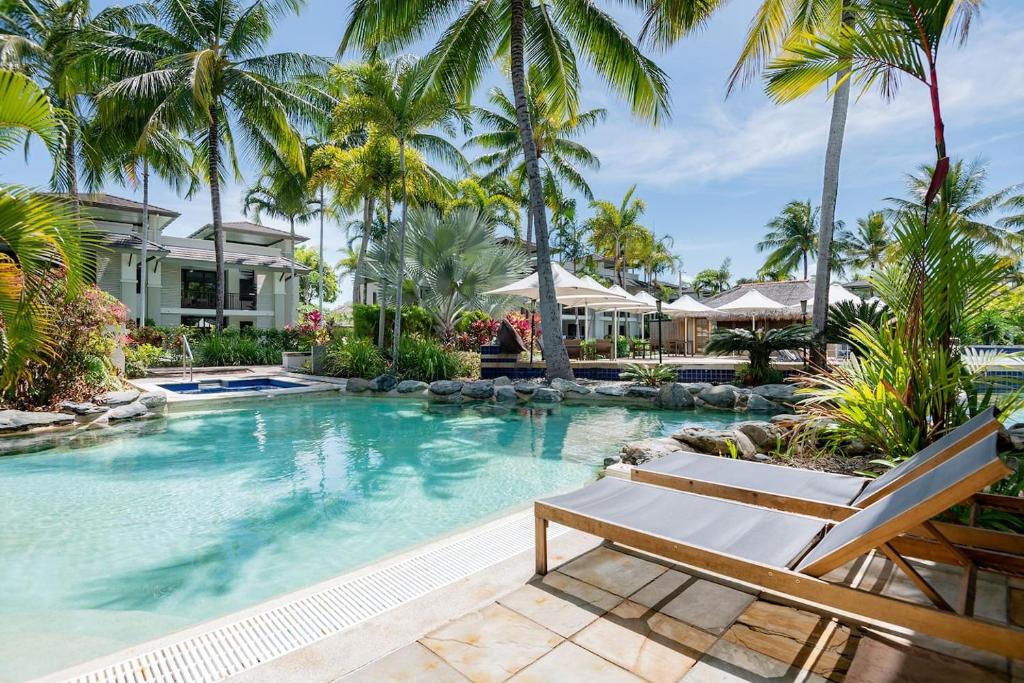 a swimming pool with palm trees and a house at Poolside Relaxation - Resort Retreat with Beach Access in Port Douglas