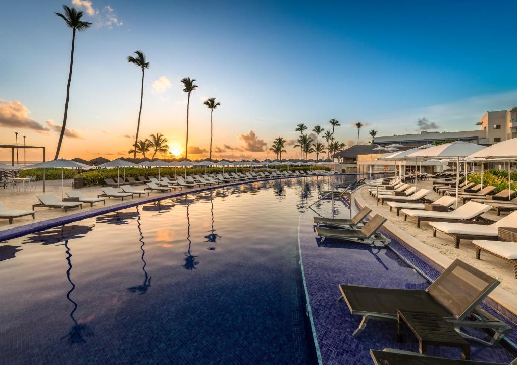 Pool deck at sunset with loungers, umbrellas, and palm trees.