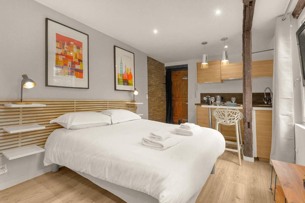 une chambre avec un grand lit blanc et une cuisine dans l'établissement Le Studio des Antiquaires - Studio climatisé, à Toulouse