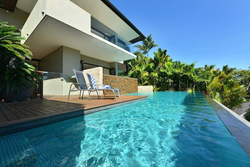 a swimming pool with two chairs and a house at 61 Murphy Street - Luxury Holiday Home in Port Douglas