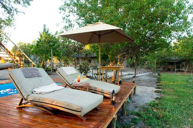 2 camas en una terraza de madera con sombrilla en Candies Vacation Cottage Khwai, en Khwai