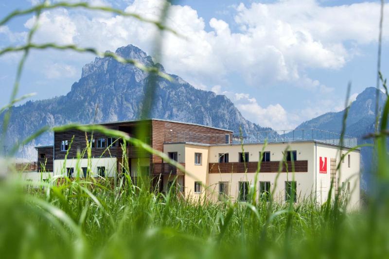 a building with a mountain in the background with green grass at Apartmenthotel 's Mitterndorf in Traunkirchen