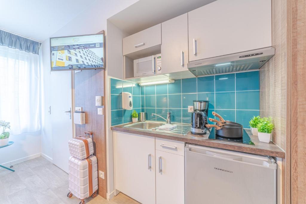 a kitchen with white cabinets and blue tiles at Break &amp; Home Paris Italie Porte de Choisy in Ivry-sur-Seine