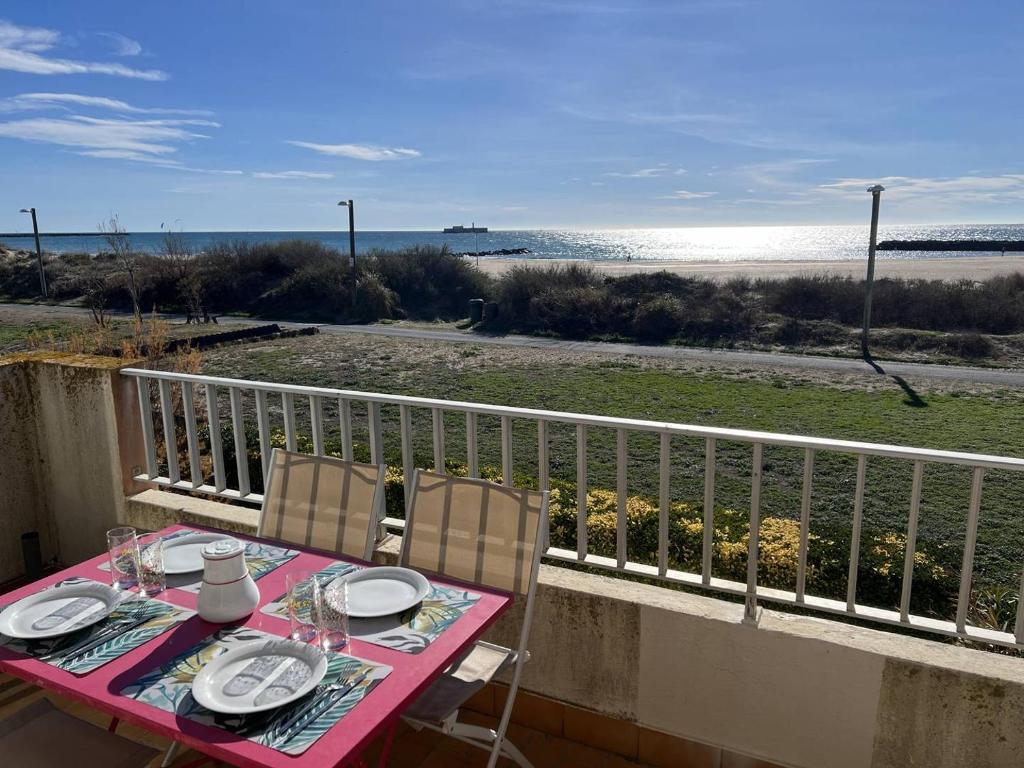 une table rose avec des chaises sur un balcon donnant sur la plage dans l'établissement MAISONS SUR LA PLAGE Joli 3 pièces mezzanine 1ère ligne vue mer Richelieu Cap d'Agde, au Cap d'Agde