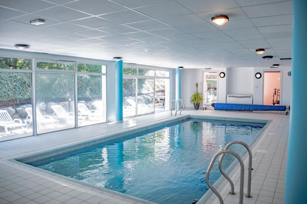 a large pool with blue water in a room with windows at Residence Le Royal Golf & Horse in Mooslargue