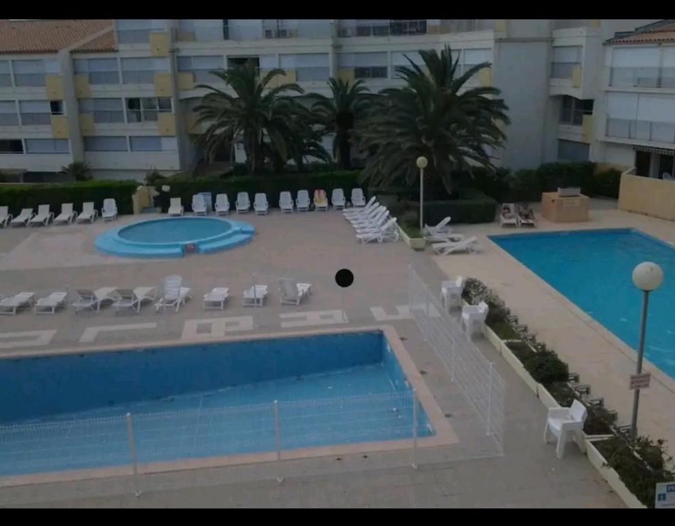 - une vue sur une piscine avec des chaises et un bâtiment dans l'établissement Jolie appartement avec piscine privé, au Cap d'Agde