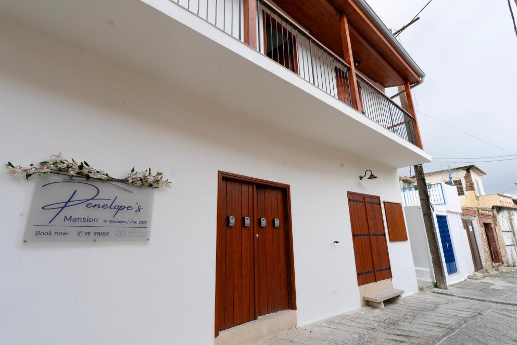 a white building with wooden doors and a sign on it at Penelope's Mansion Omodos in Omodos