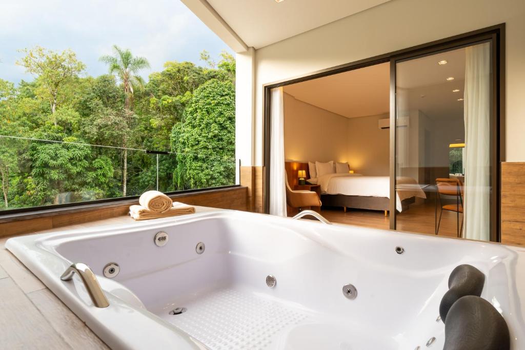 a bathtub in a bathroom with a view of a bedroom at Vert Hotel Penedo in Penedo